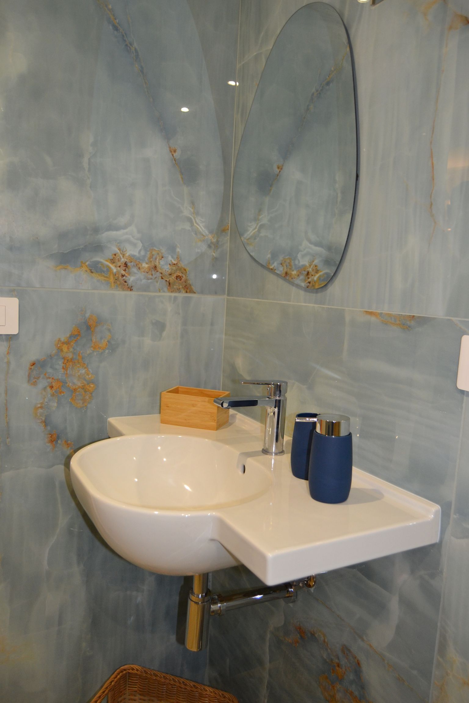 Piccolo lavabo da bagno con specchio a parete, pareti piastrellate di blu e articoli da toeletta sul ripiano.