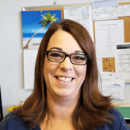 A woman wearing glasses is smiling in front of a bulletin board