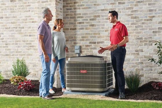 A man in a red shirt is talking to a couple in front of a brick building.