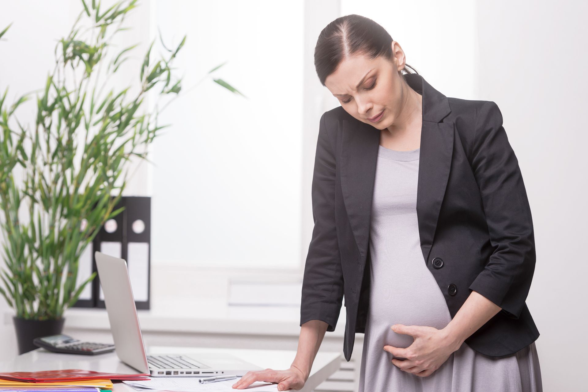a pregnant woman is standing in front of a laptop