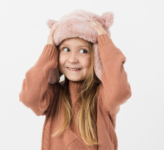 Niña con un gorro rosa de piel sintética con orejas y un suéter a juego, sonriendo.