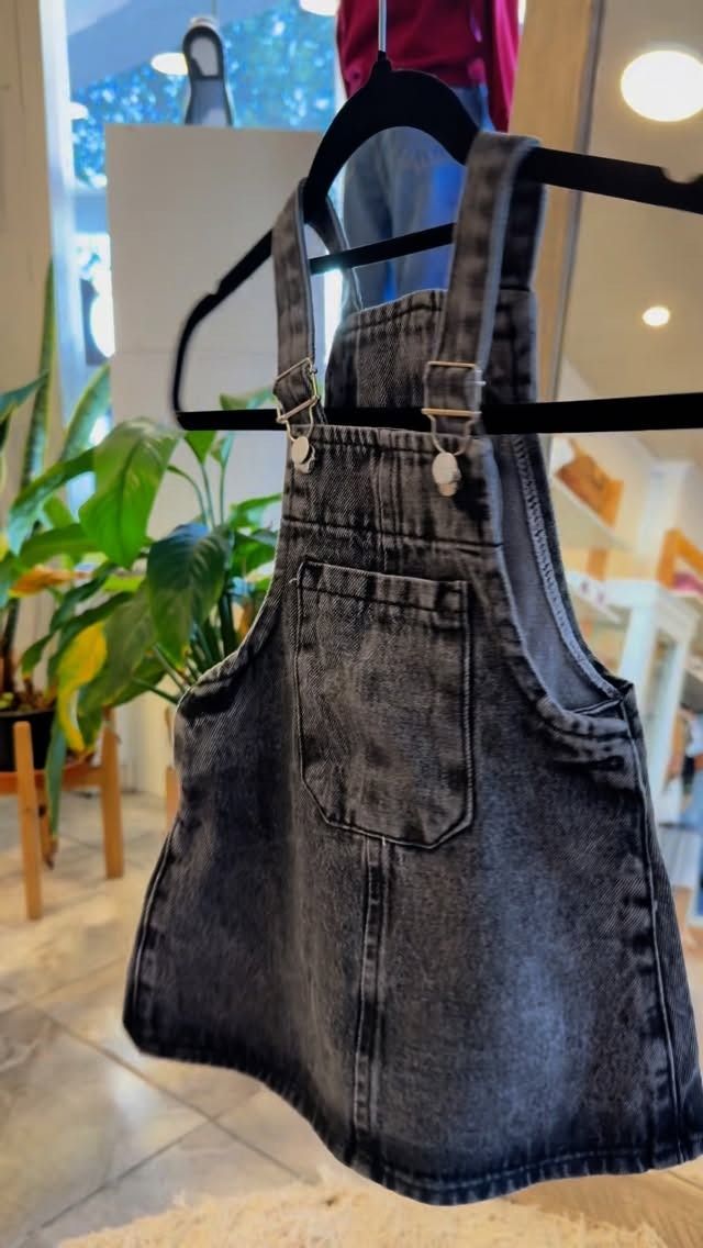 Vestido vaquero gris de peto colgado en una percha negra.