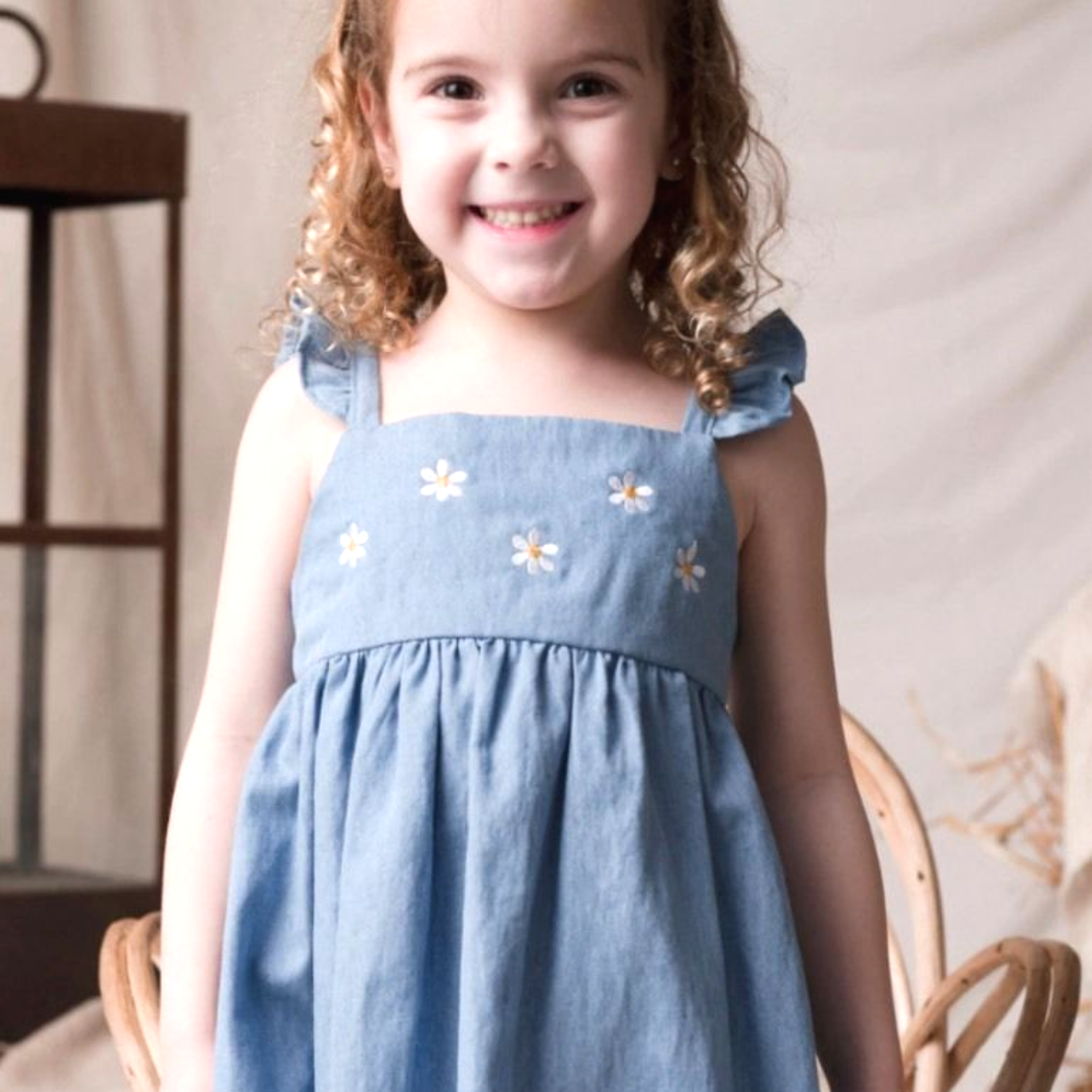 Una niña que lleva un vestido azul con bordados de margaritas sonríe sentada.
