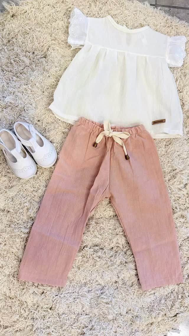 Pantalones rosas, blusa blanca y zapatos blancos sobre una alfombra blanca.