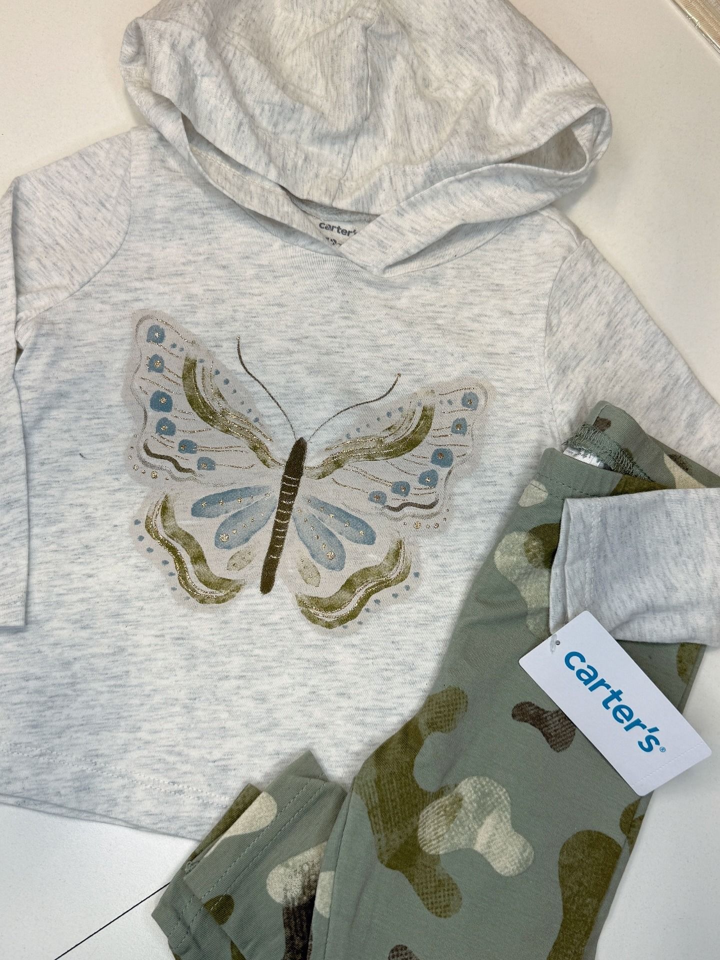 Sudadera gris con capucha y estampado de mariposas, y leggings verdes de camuflaje, marca Carter's.