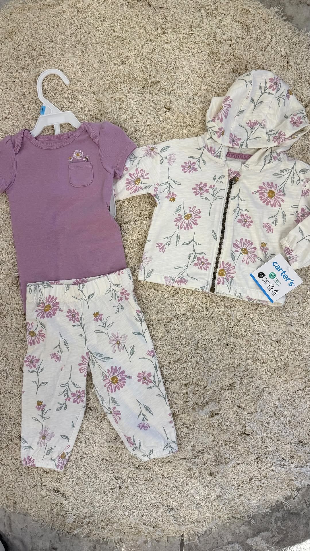 Conjunto de body morado y pantalón/chaqueta blanca con estampado floral para bebé sobre una alfombra.