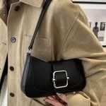 Bolso bandolera negro con hebilla plateada en una persona que lleva una chaqueta color canela.