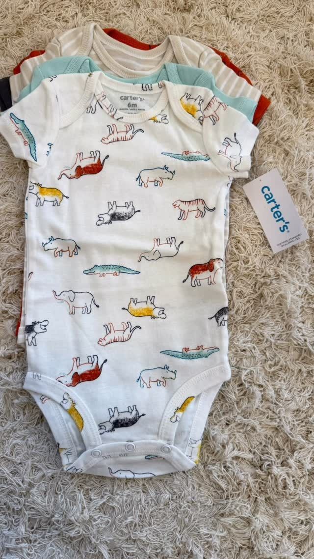 Tres bodies de bebé sobre una alfombra beige. Uno blanco con estampado animal de colores, dos a rayas. Etiqueta de Carter's.