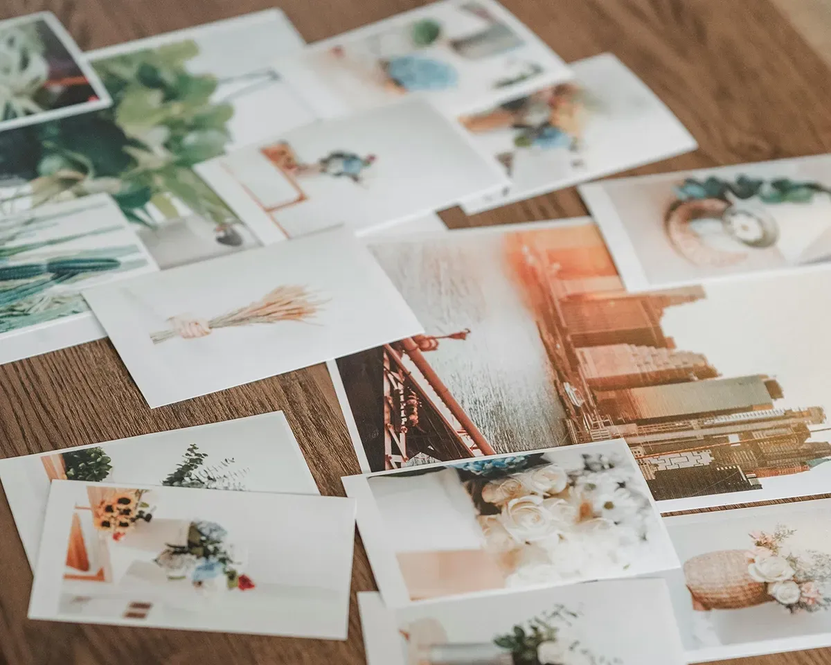 Hundreds of photographs spread out on a table alongside a plant, coffee mug and strip of film.