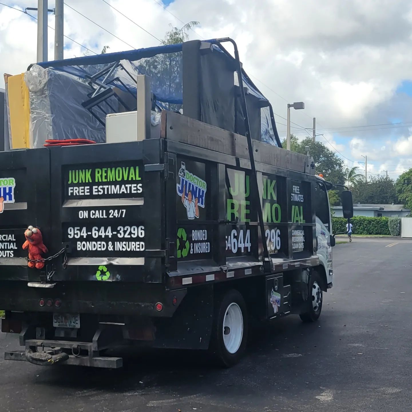 Junk removal truck loaded with items, parked on a street; black truck with green and white lettering.