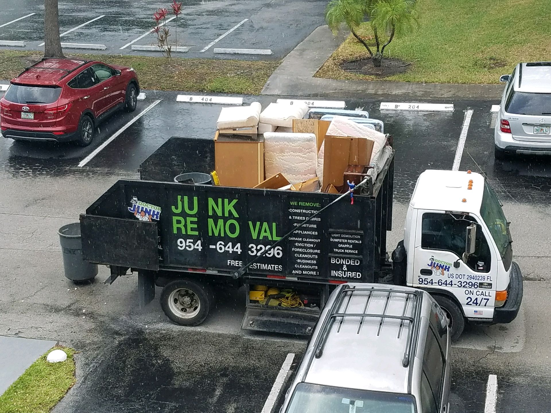 Junk removal truck loaded with furniture in a parking lot on a rainy day.