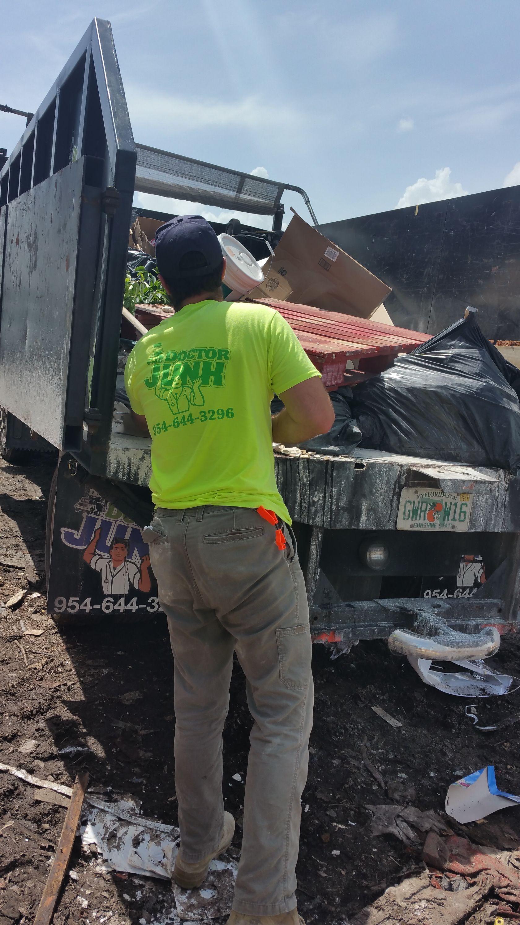 Man in yellow shirt loading debris into a dump truck on a sunny day.