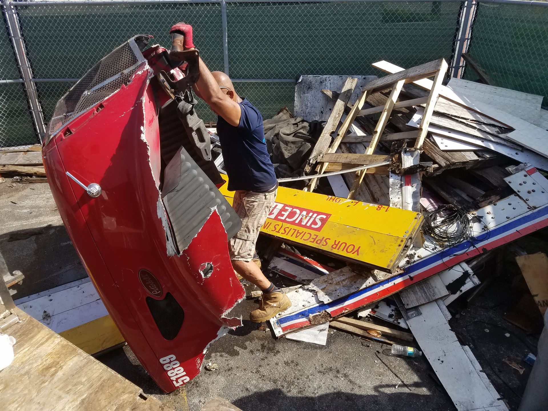 Man lifting red car door in a debris-filled outdoor lot.