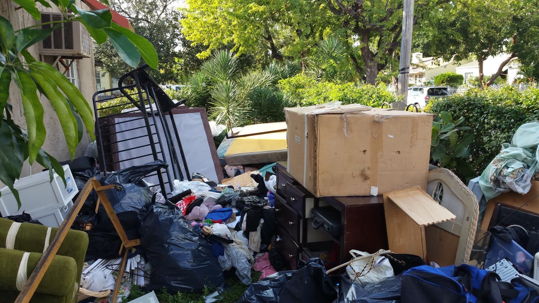 Pile of discarded furniture and trash in a yard, including mattresses, boxes, and bags.