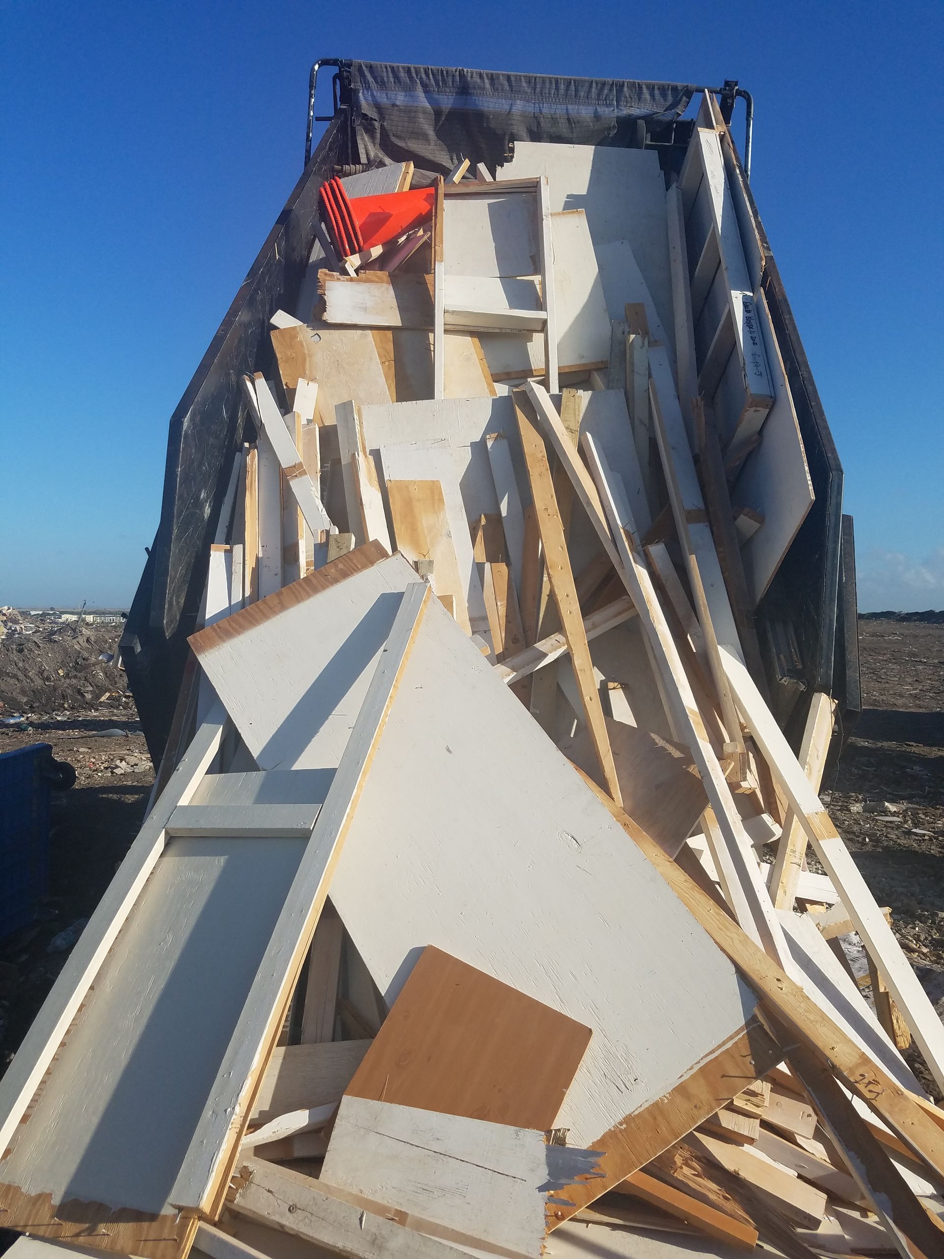 A truck bed filled with construction debris, including wood and white panels, against a blue sky.