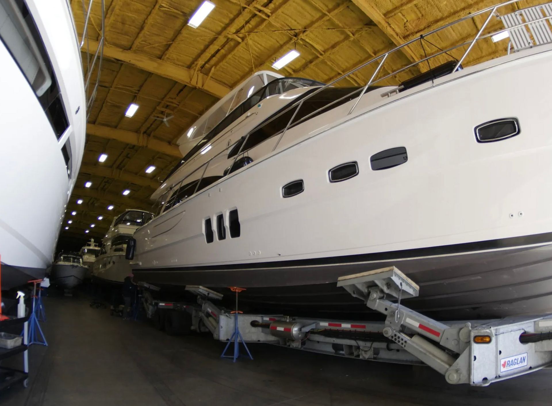 A large white boat is sitting on a trailer in a warehouse.