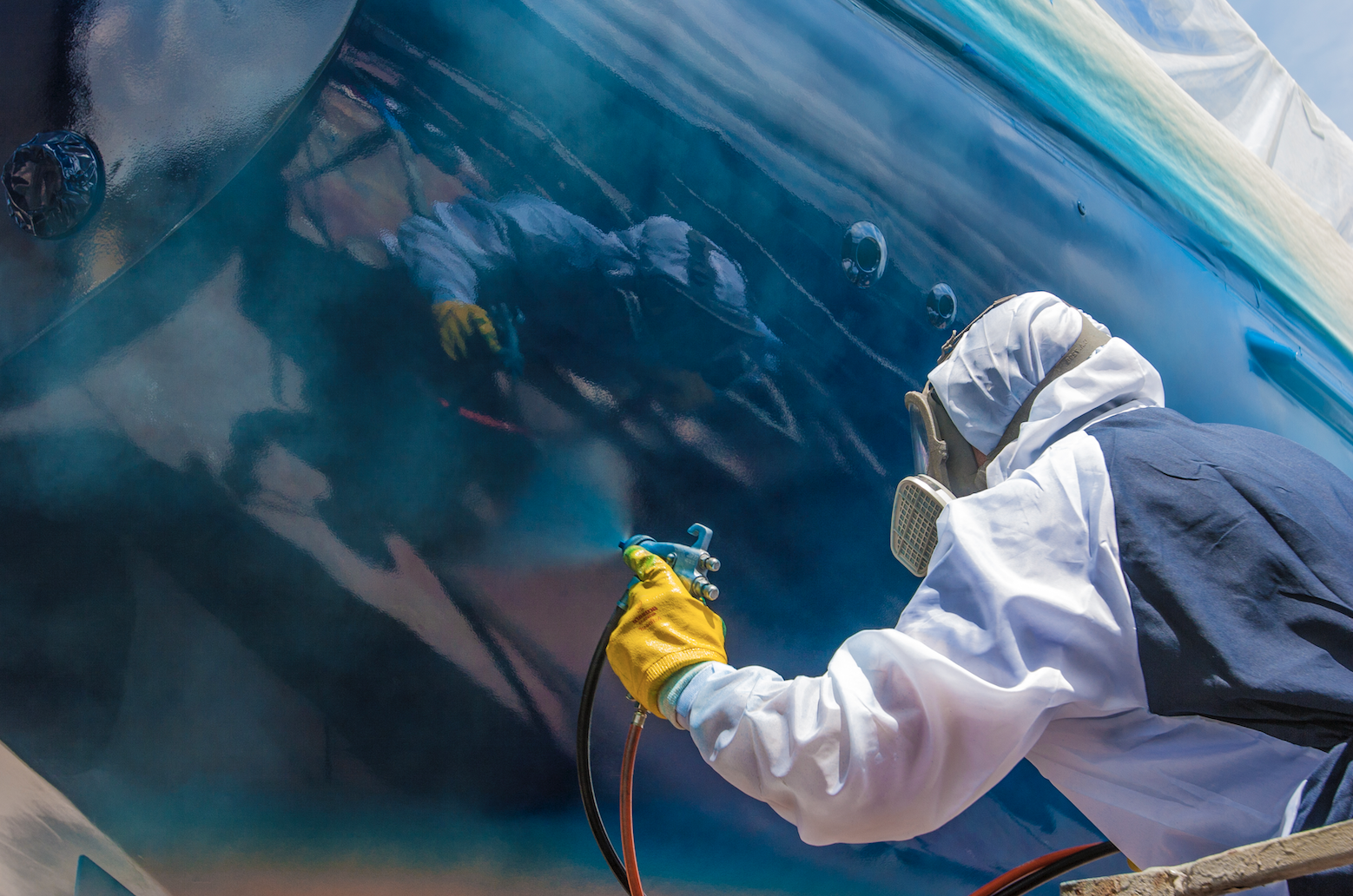A man is spray painting the side of a boat.