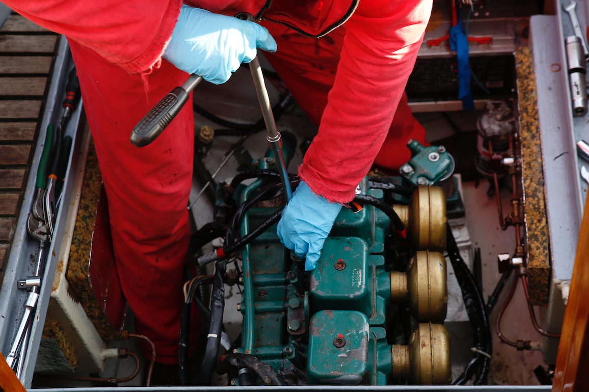 A man in red pants is working on a boat engine