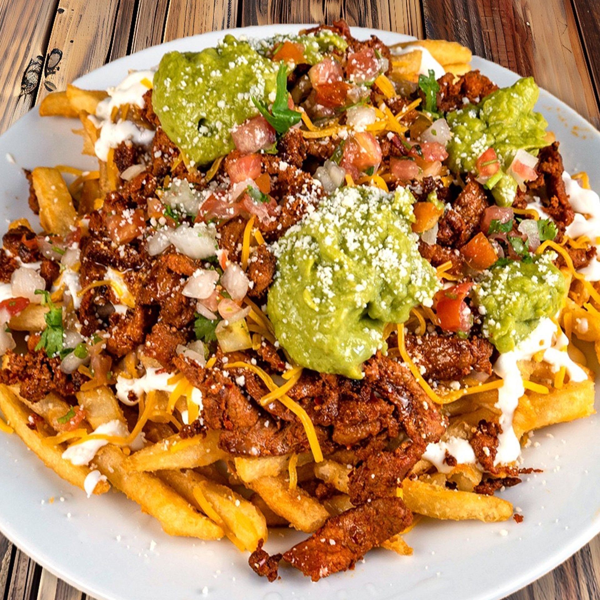 Fries topped with meat, cheese, guacamole, and salsa on a white plate.