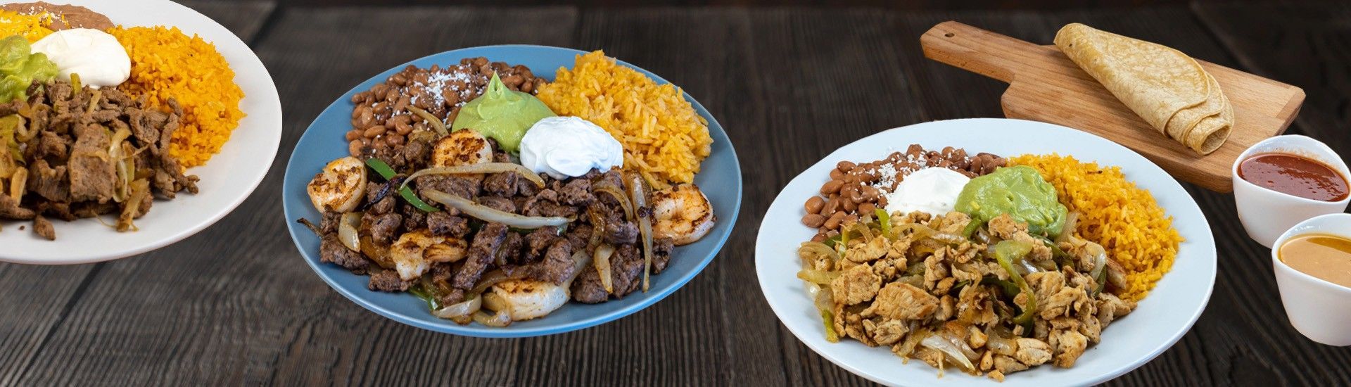 Plates of Mexican food, including meat, rice, guacamole, and sour cream. Tortillas and sauces on the side.