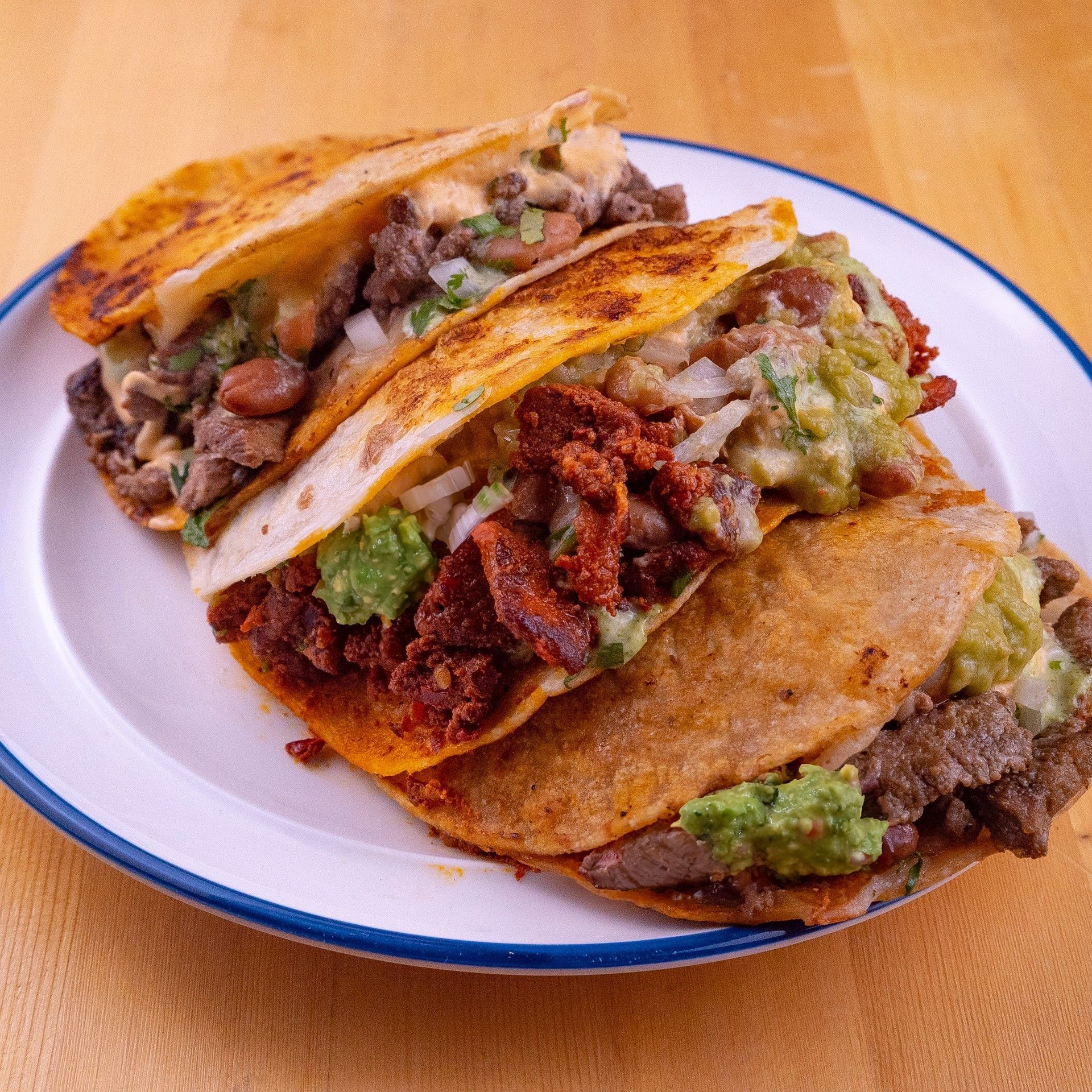 Three tacos on a plate: filled with meat, guacamole, onions, and beans.
