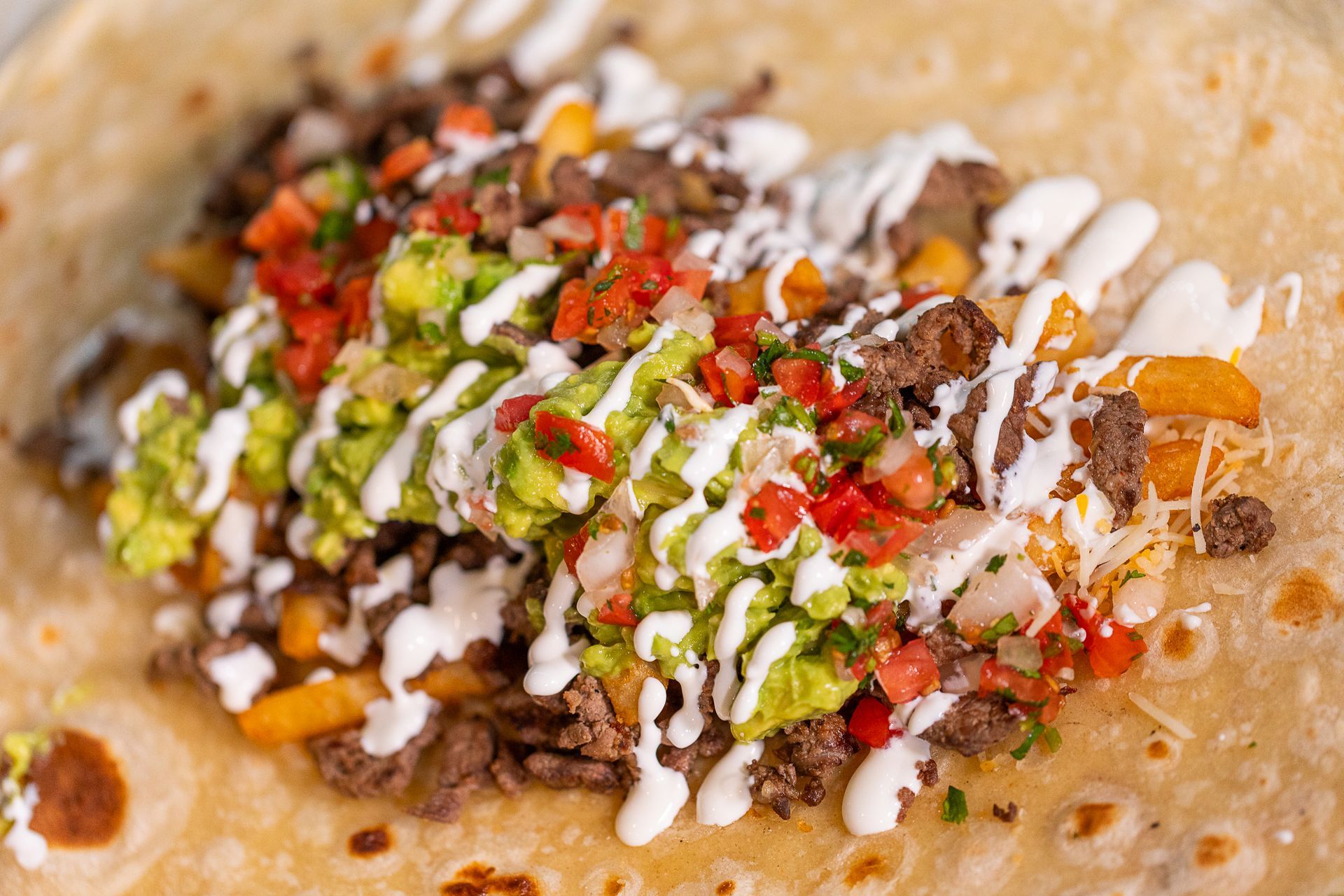 Burrito with meat, guacamole, salsa, fries, and cream drizzled on a tortilla.