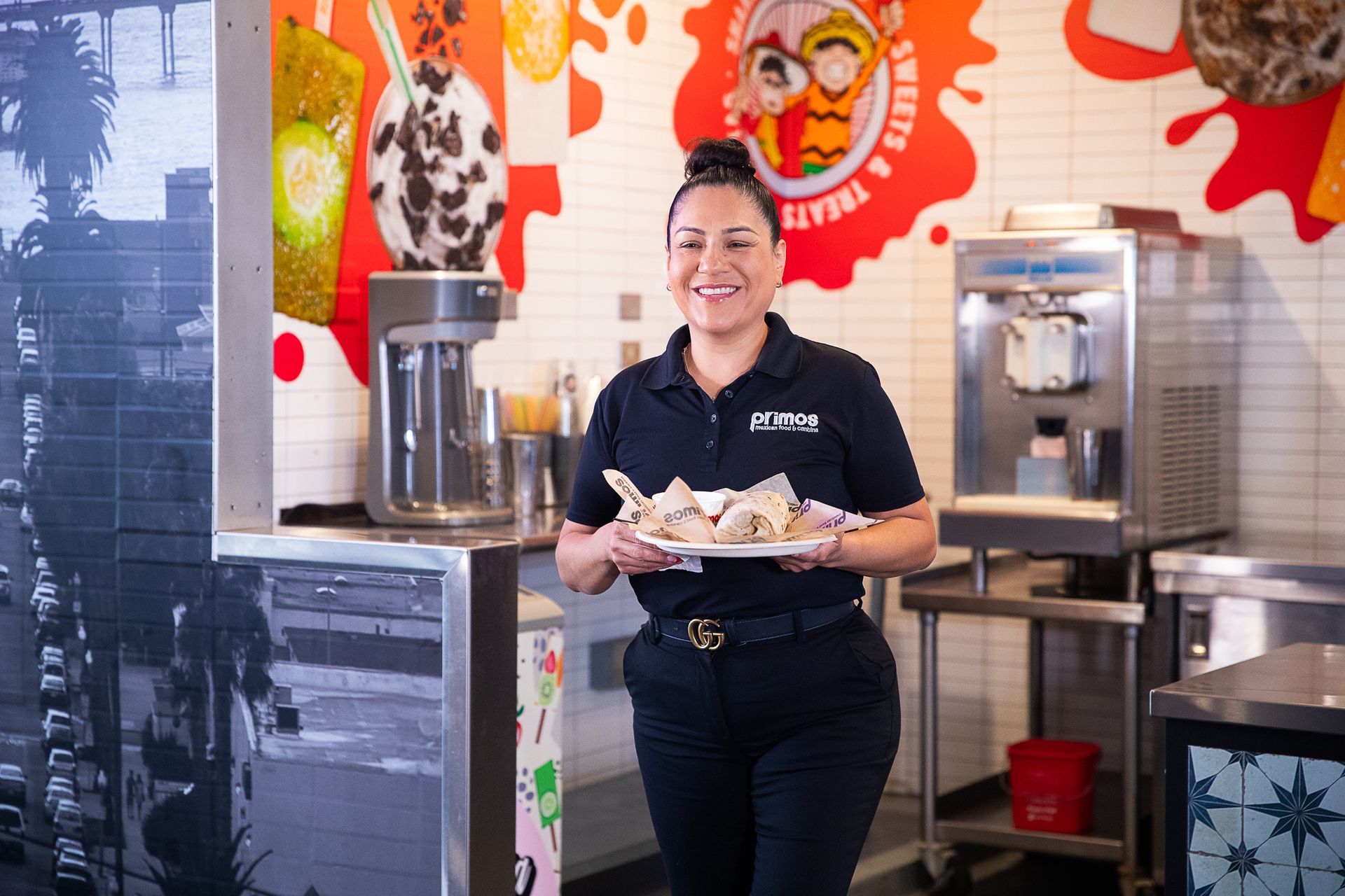 Woman in black uniform holding dessert plate, smiling in dessert shop.
