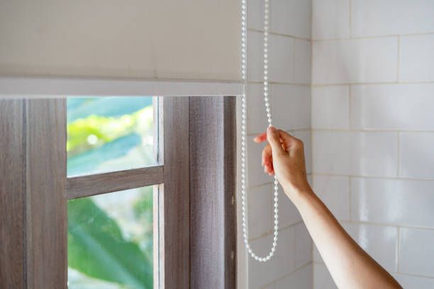 A person is pulling a cord to open a window blind.