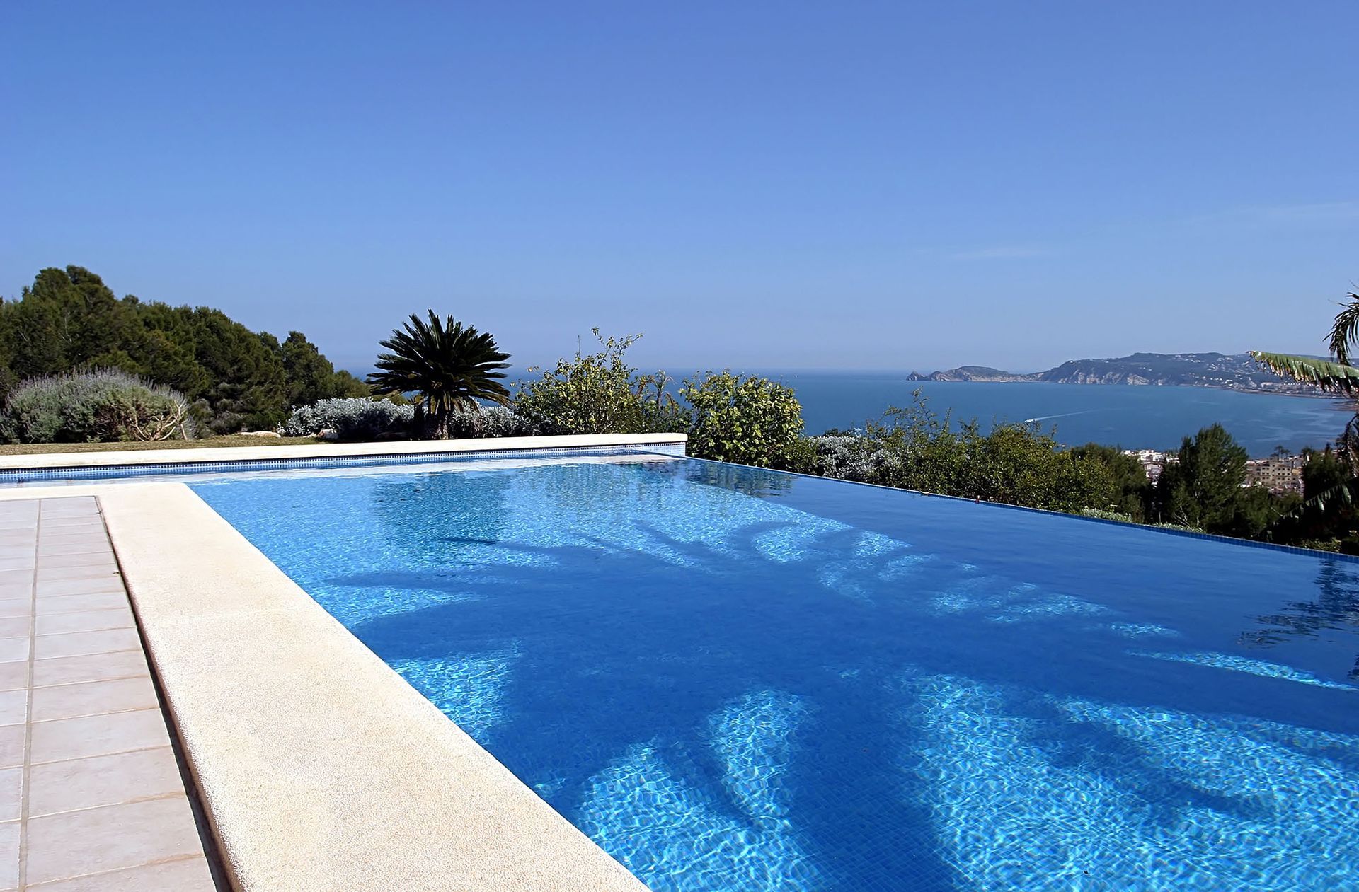 A blue infinity pool overlooks the ocean on a sunny day.