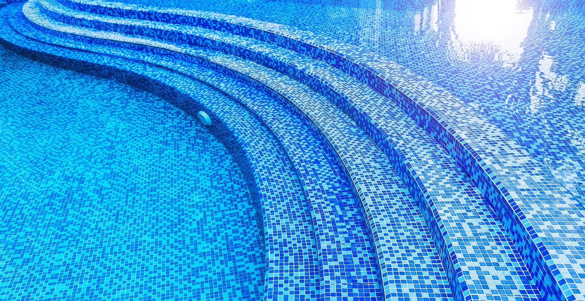 Blue-tiled pool with curved steps, reflecting sunlight.