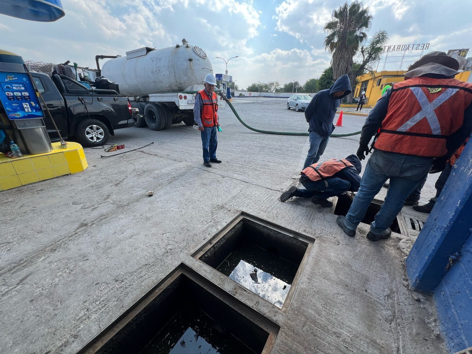 Los trabajadores cerca de un desagüe de alcantarillado abierto están utilizando una manguera conectada a un camión cisterna.