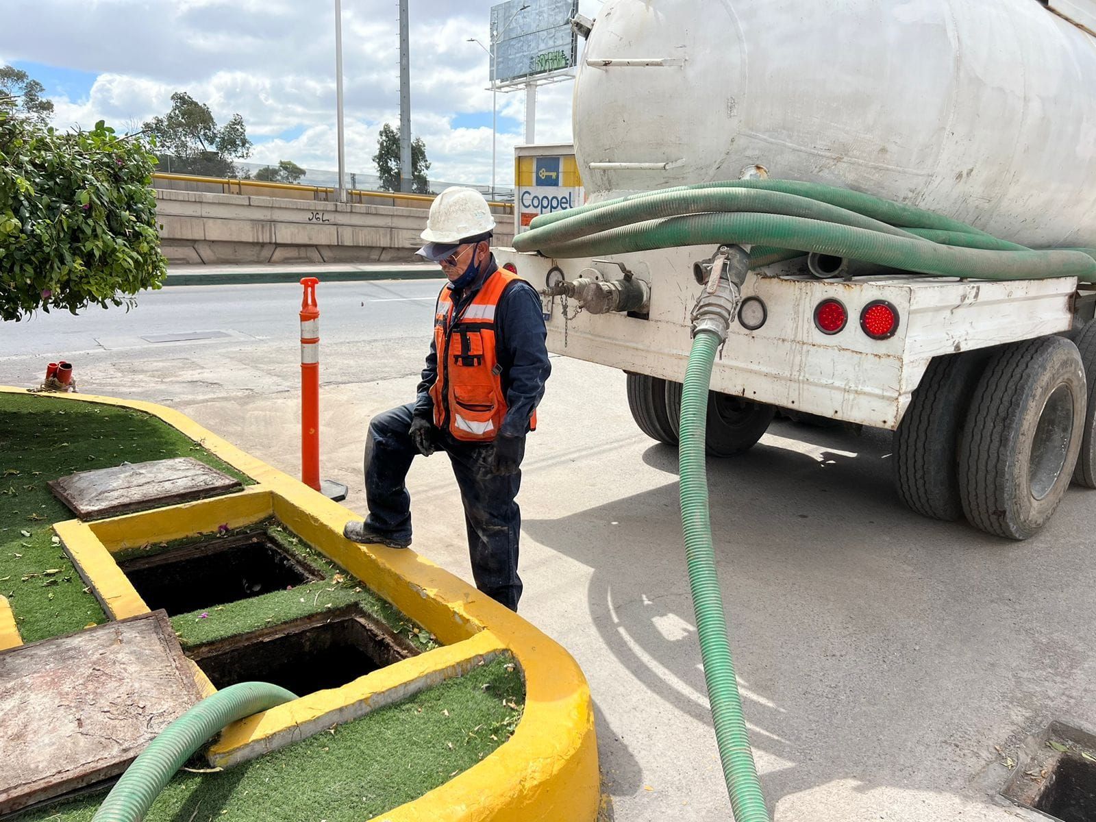 Un hombre con chaleco de seguridad revisa el tanque de aguas residuales conectado a un camión en un entorno urbano.