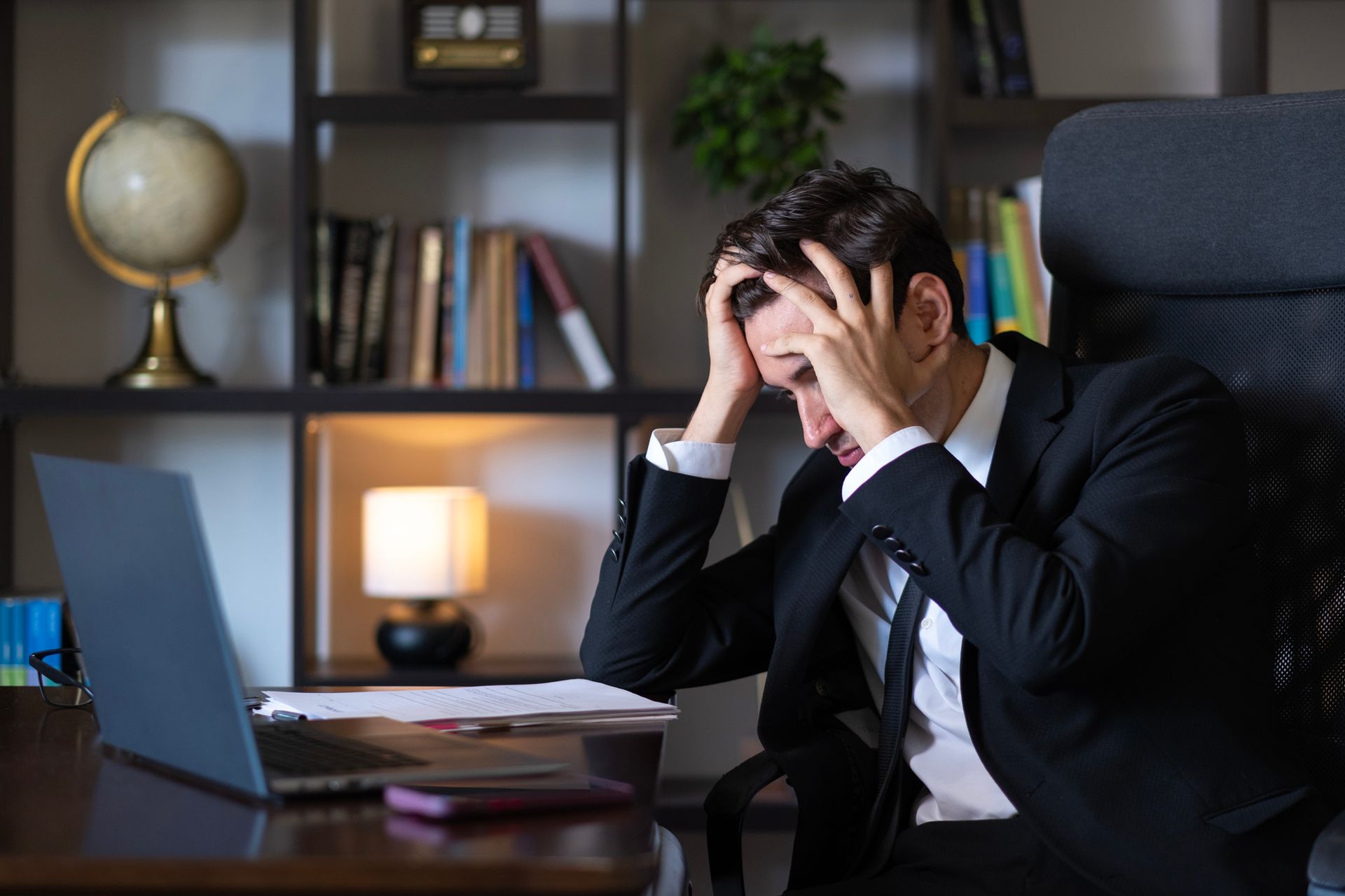 A woman is sitting at a table with her hands on her head.