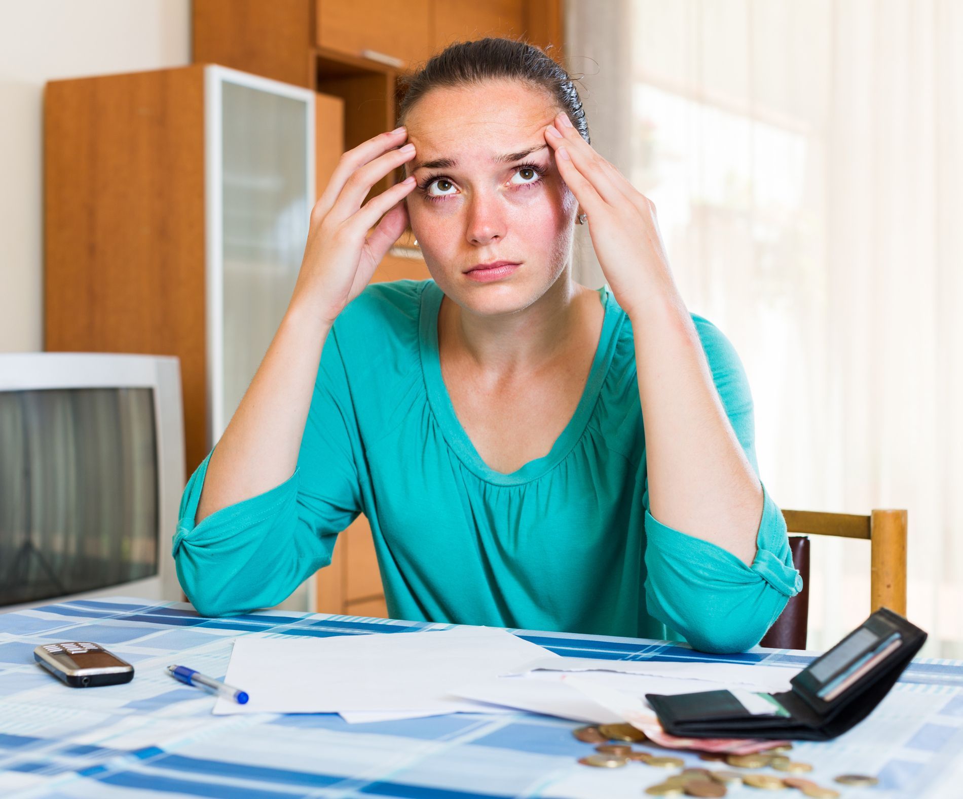 A woman is sitting at a table with her hands on her head.
