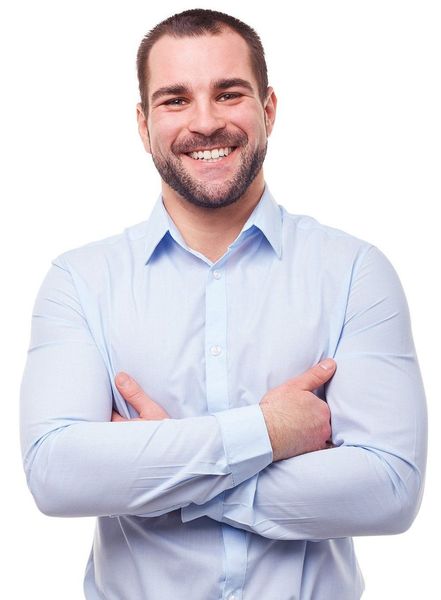 A man in a light blue shirt is smiling with his arms crossed