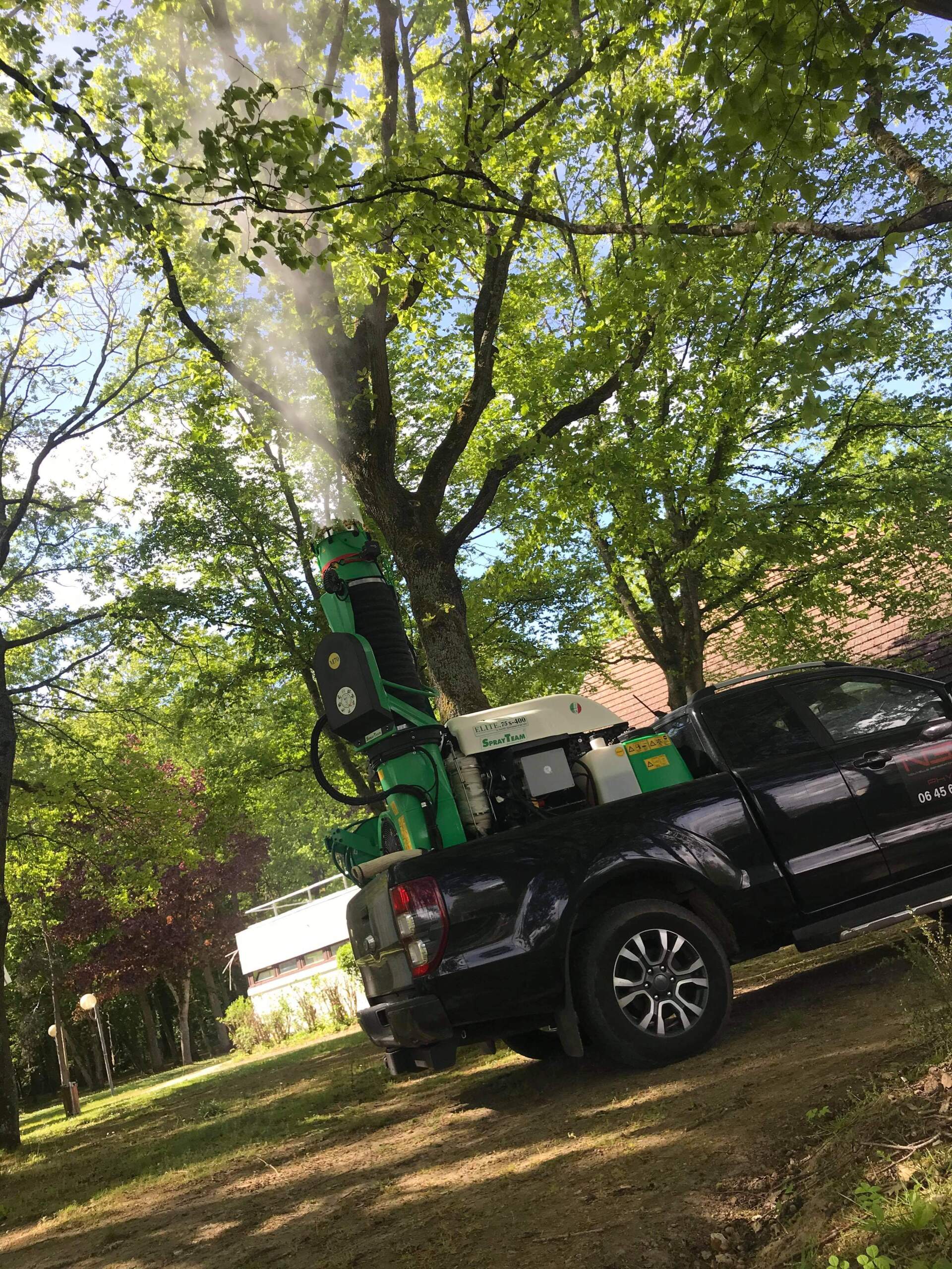 Un camion pulvérise des arbres avec une machine à l'arrière.