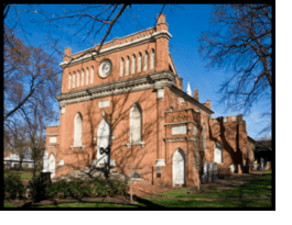 Red brick Gothic-style church building with tall arched windows under a blue sky