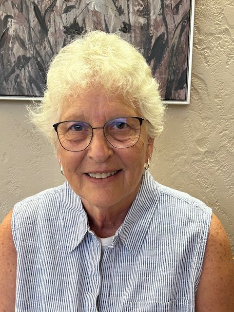 Woman with glasses smiling, wearing a blue striped top, indoors.