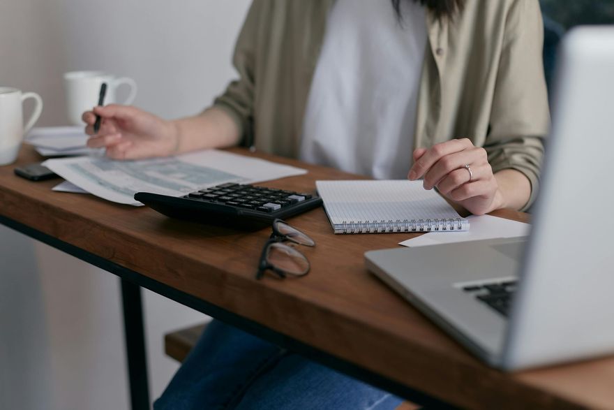 Woman working at a desk with laptop, calculator, and papers, writing notes.