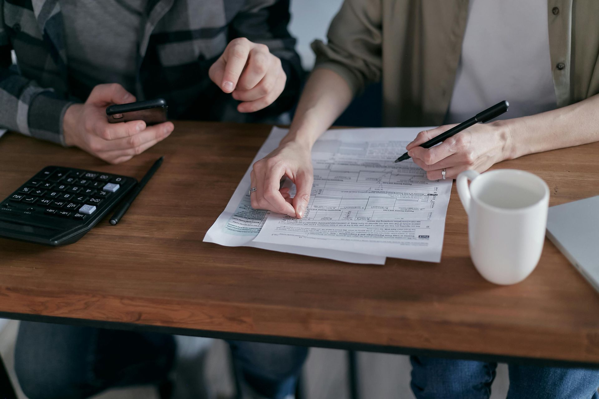 Two people reviewing documents, using a calculator and pen, seated at a wooden table.