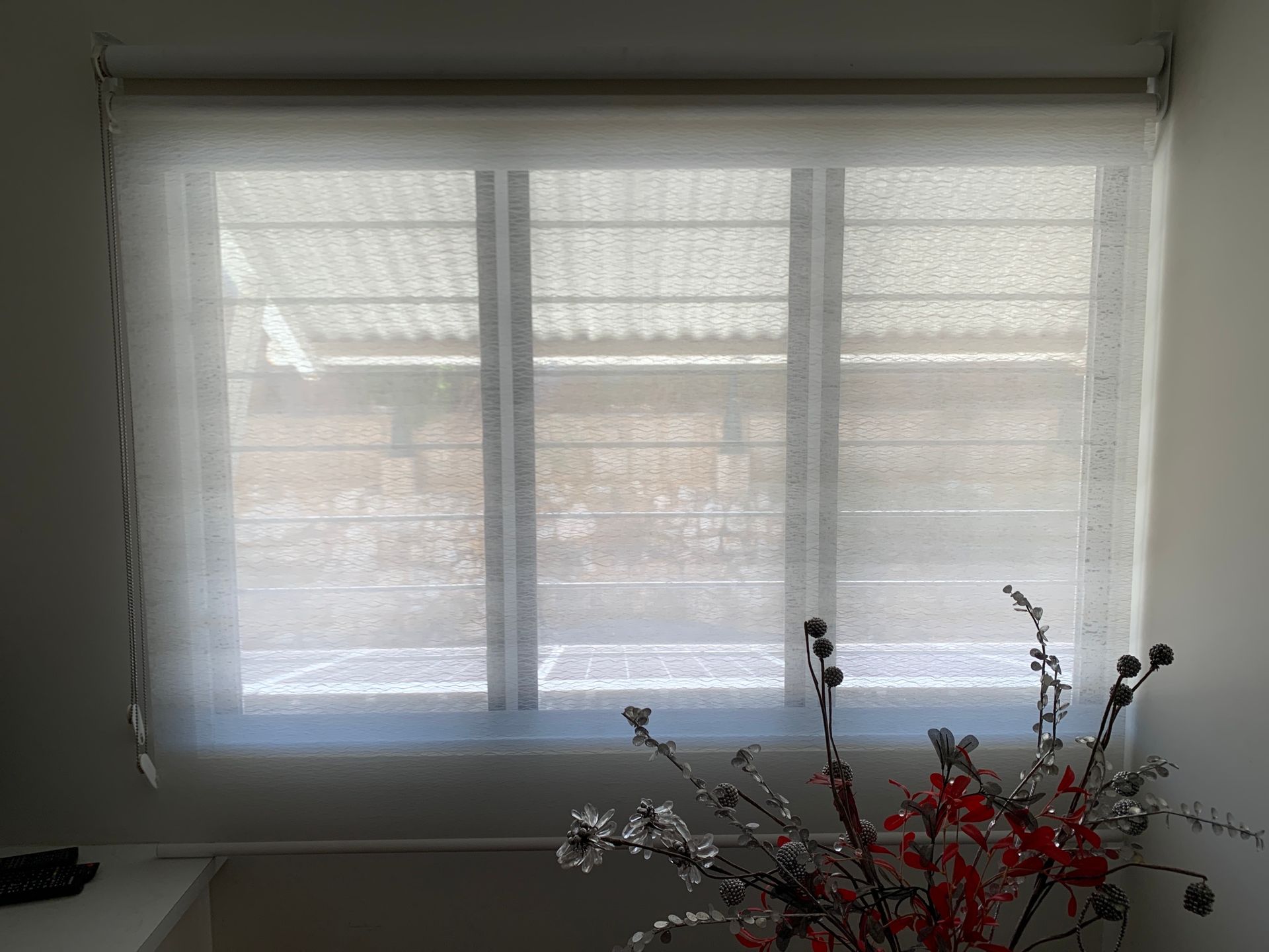 A window with white blinds and a vase of flowers in front of it.