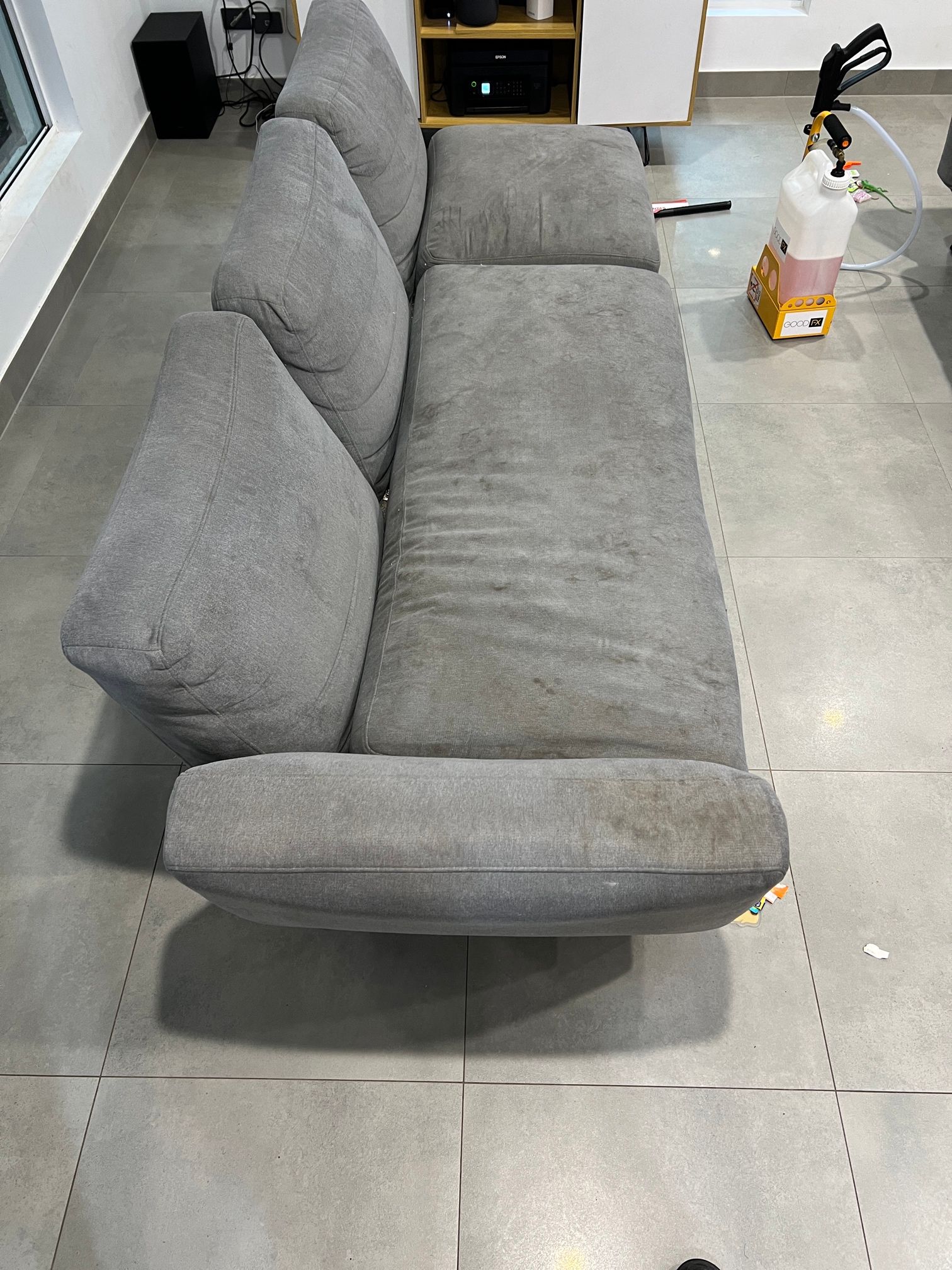 A grey couch is sitting on a tiled floor in a living room.