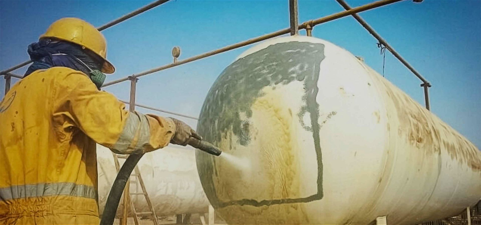 A man in a yellow suit and hard hat is cleaning a large tank.