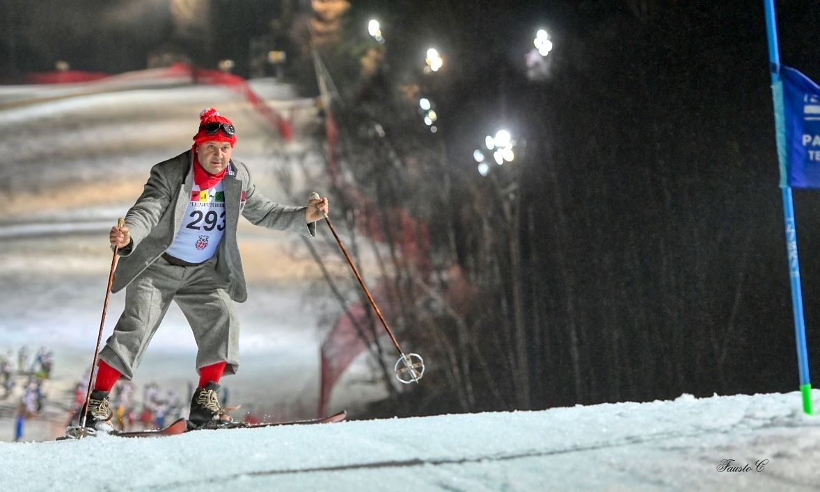 Un uomo in giacca e cravatta e cappello rosso sta sciando lungo una collina innevata.