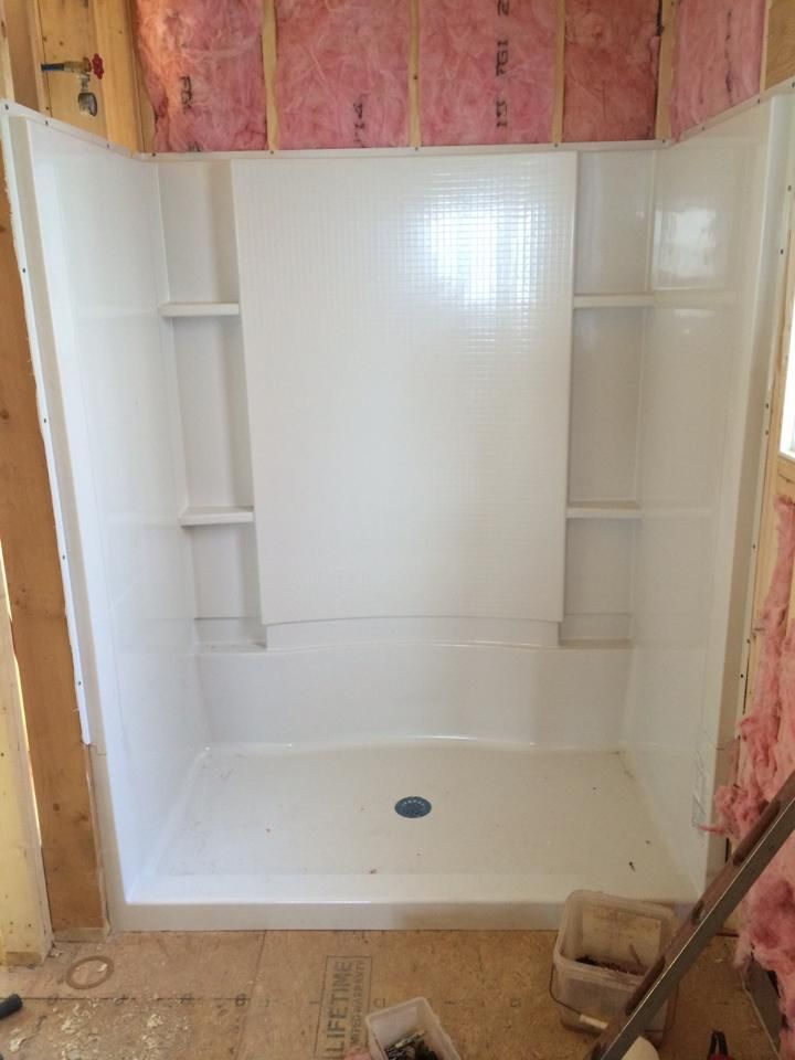 A white shower stall with shelves in a bathroom under construction.