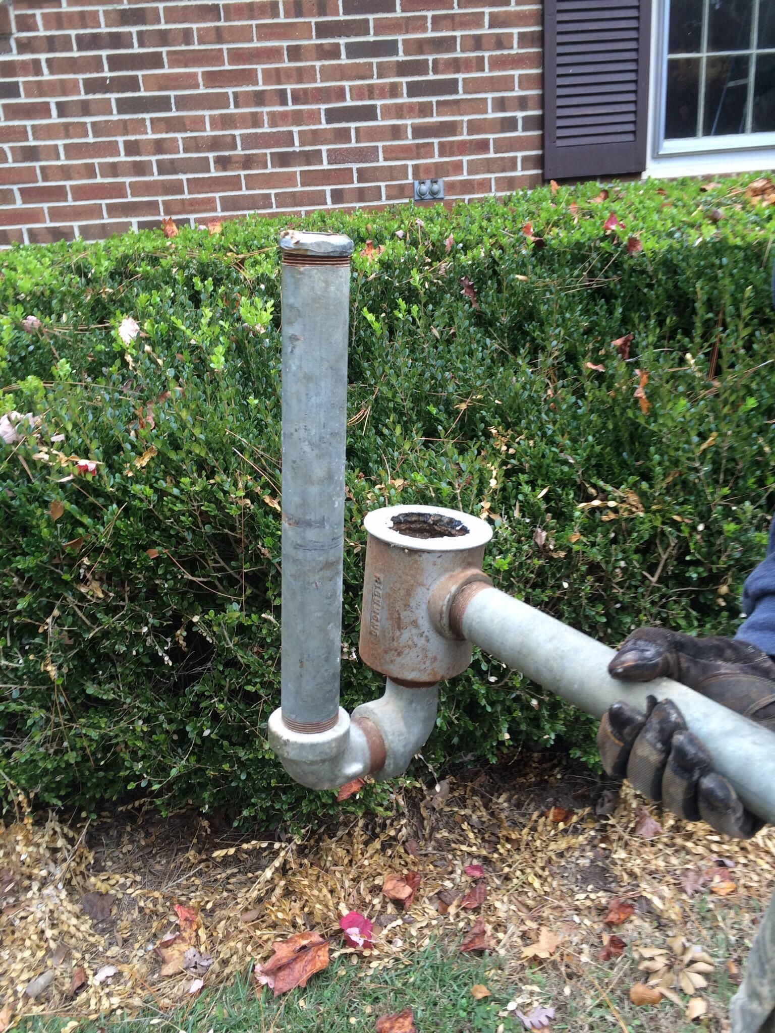 A person is working on a pipe in front of a brick house.