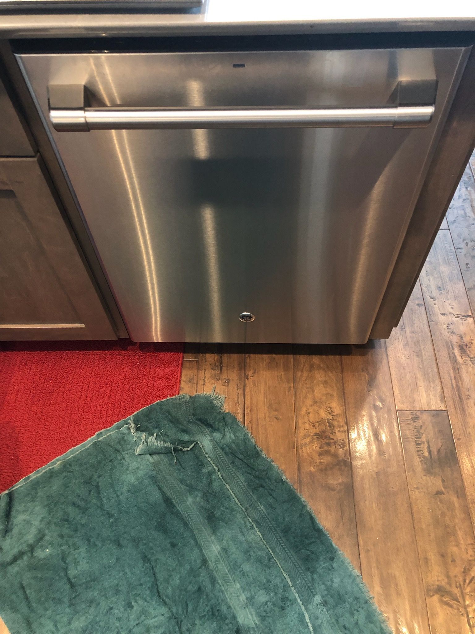 A stainless steel dishwasher is sitting on a wooden floor in a kitchen.