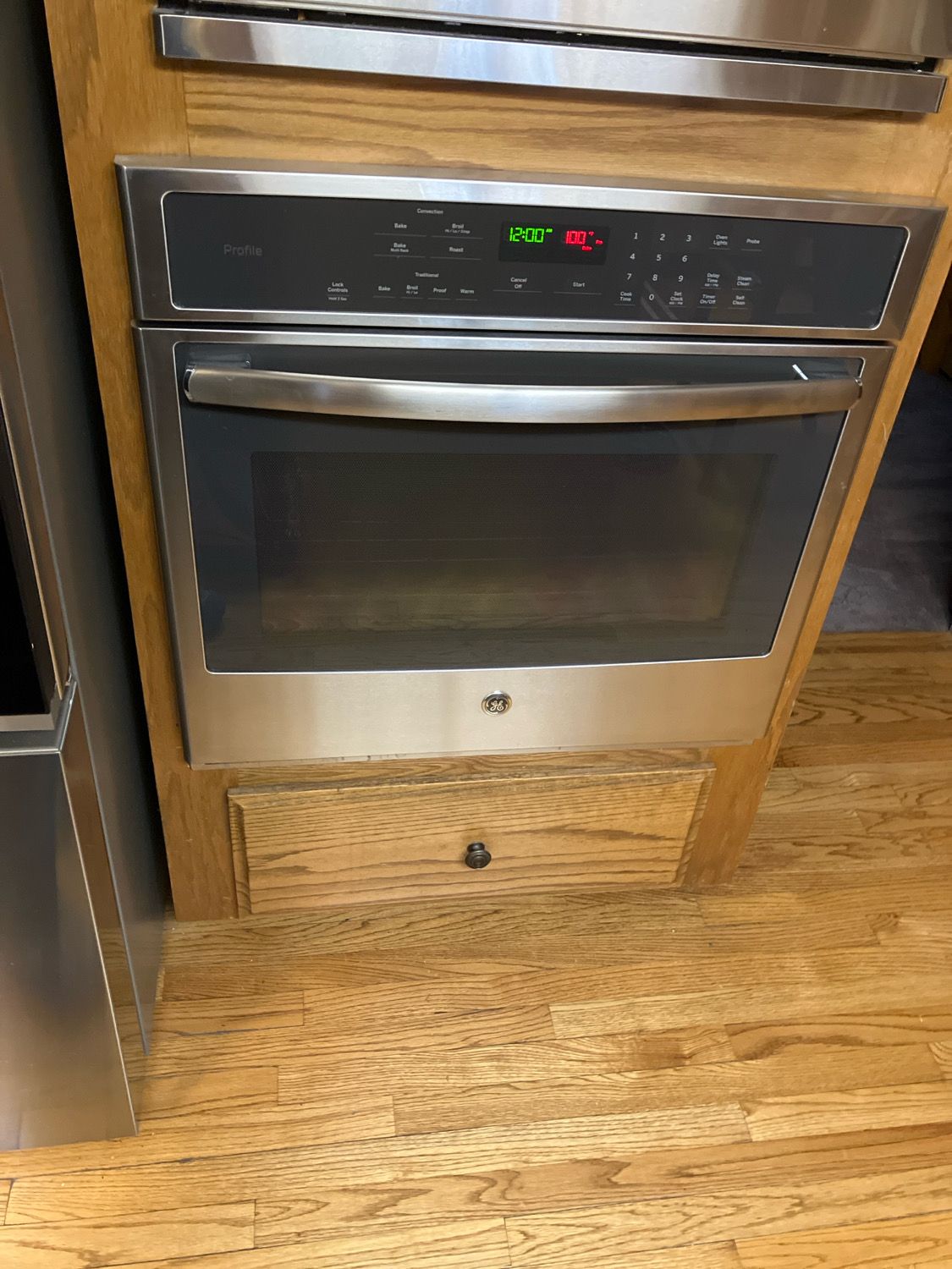 A stainless steel oven is sitting on top of a wooden cabinet.