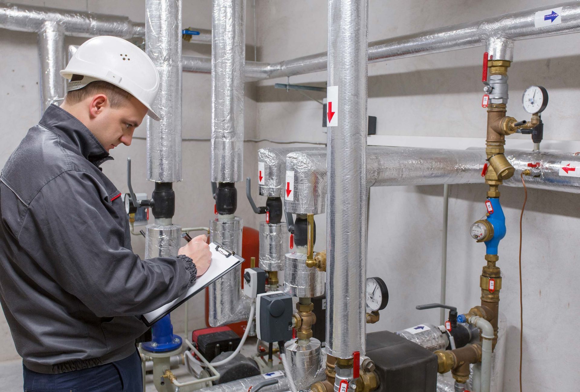 A technician in a hard hat inspects heating system in boiler room.