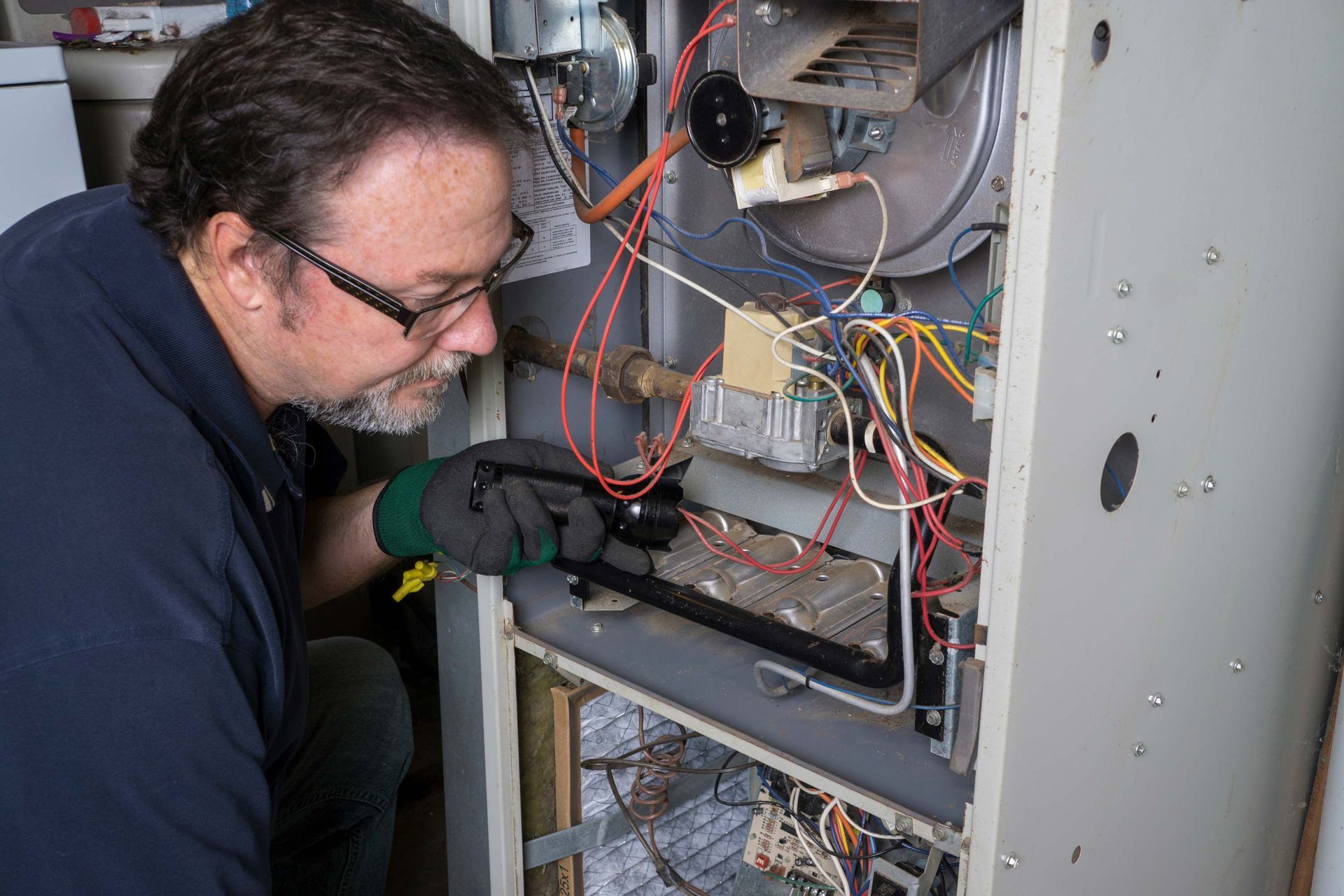 A male technician checks the inside cabling and components of a furnace.